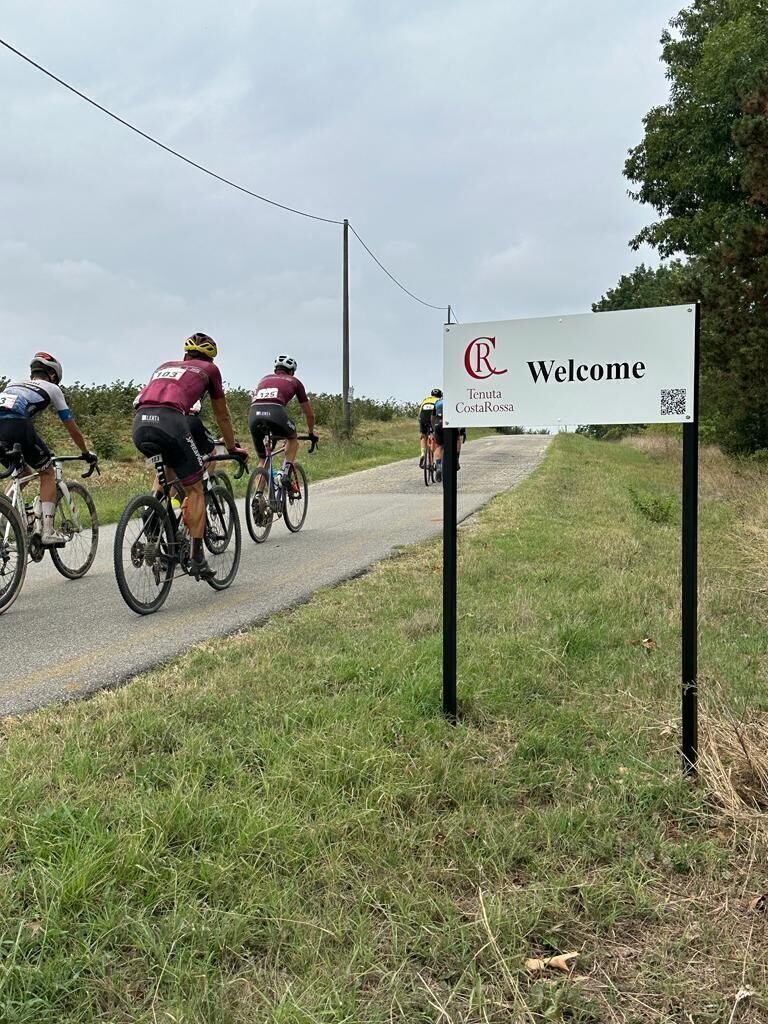 Cyclists passing Tenuta CostaRossa Welcome sign